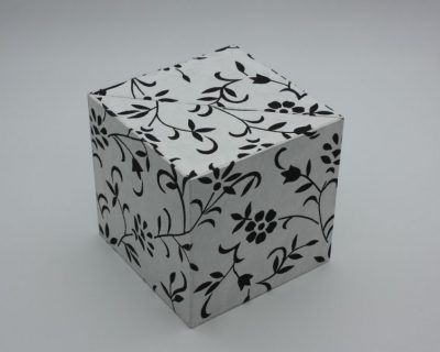 Caja en forma de cubo y apertura de concha. Exterior en papel artesano decorado, cajones e interior en Geltex. Artículo hecho a mano.
